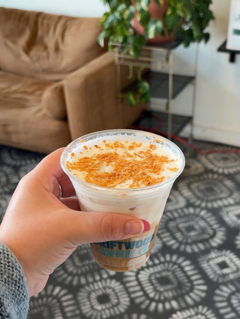A hand holds the Crazy Coconut coffee drink from Driftwood Coffee Co.