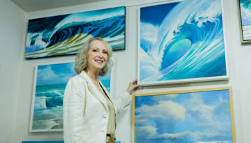 Artist Melissa Mitchell stands in front of her artwork of waves and oceans.
