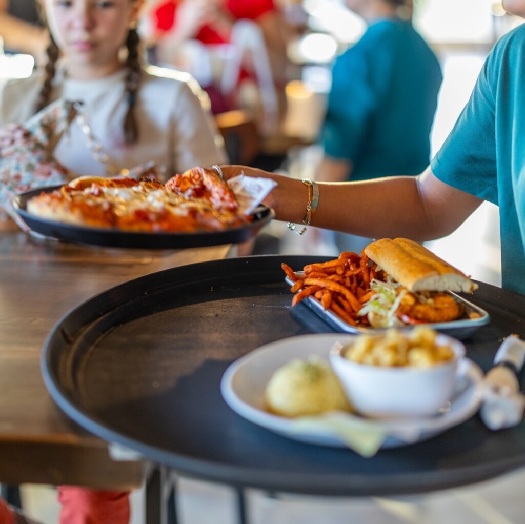 A server brings out various plates of food including a sub, pizza and mac and cheese inside Portland's Fifth & Elm.