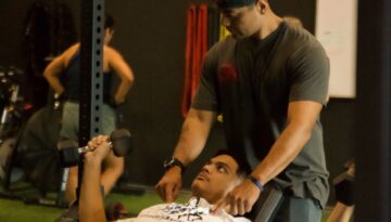 Personal trainer Alain Escobar helping a man lifting weights inside his gym AE Fitness.