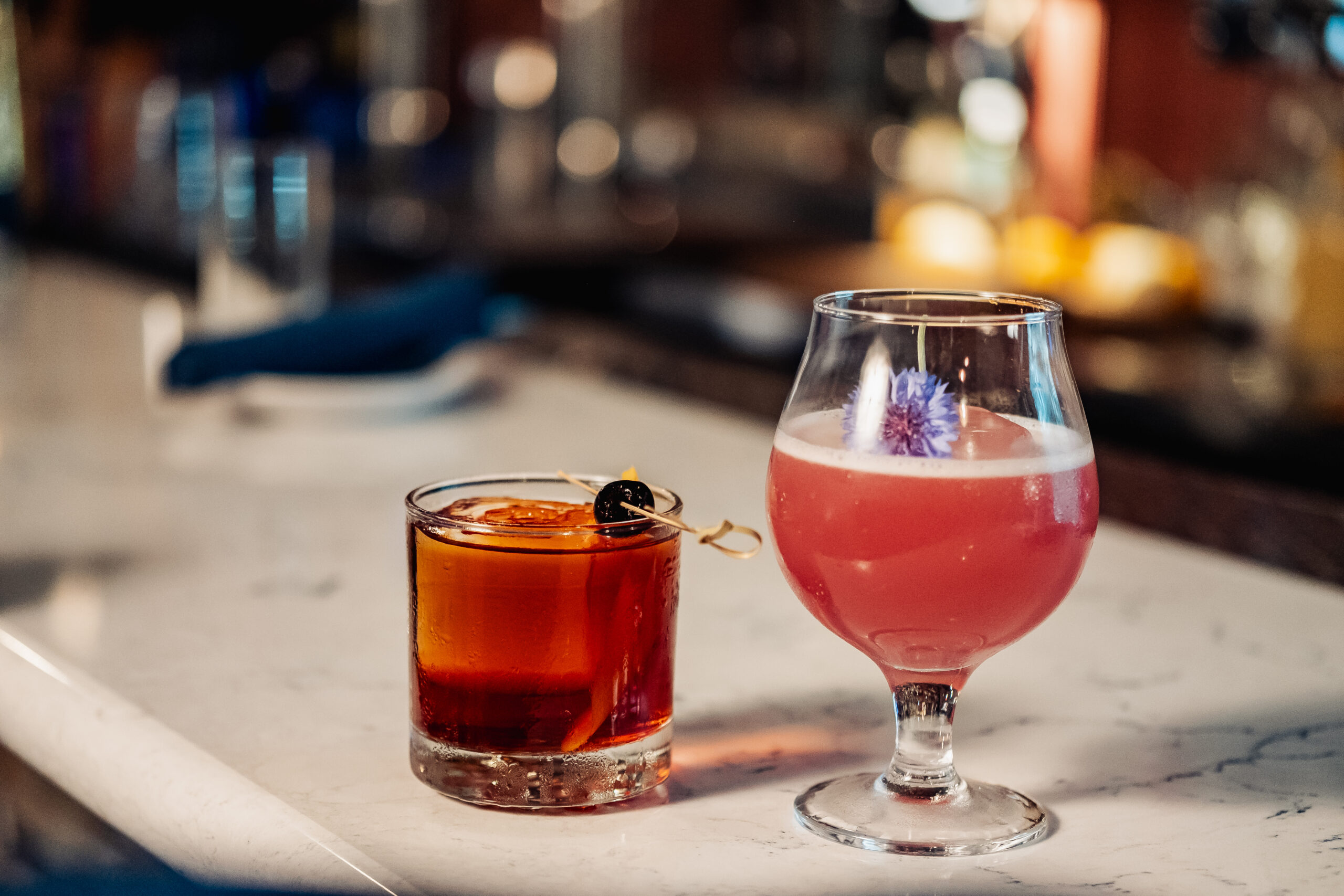 Two drinks sit on a marble countertop inside Fork & Vines.