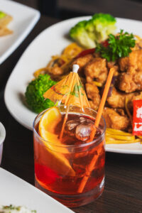 A close up on a drink with a veggie, noodle and protein meal sitting behind it, both from Kapi Honda.